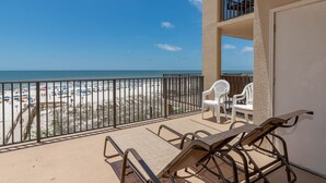 A balcony with a view of a beach, white plastic chairs, and a wooden table. - One Bedroom 3rd Floor Condo at Phoenix 5 (Orange Beach)
