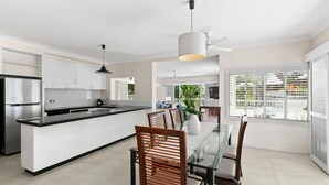 A modern kitchen with white cabinetry, a black countertop, and a dining area with a glass table and wooden chairs.