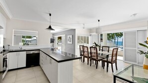 A modern kitchen with white cabinetry, a black countertop, and a dining area with wooden chairs and a glass table.