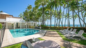 A poolside area with a clear view of the ocean, surrounded by palm trees and lounge chairs.