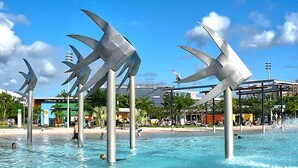 Une piscine agrémentée de grandes sculptures métalliques au centre, entourée de palmiers et surplombée d’un ciel dégagé.