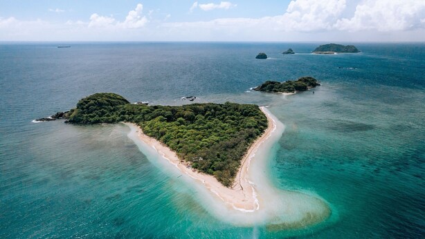Vue aérienne d’une île tropicale avec une plage étroite, entourée d’eaux turquoise cristallines et d’une végétation luxuriante.