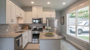 A modern kitchen with white cabinets, stainless steel appliances, a large window, and a view of the outside. - Pool/Spa, guesthouse in the heart of ATX (Austin)