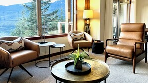 Ein gemütliches Wohnzimmer mit Ledermöbeln, einem runden Couchtisch mit Pflanze und Bergblick durch große Fenster.