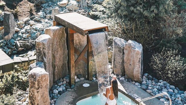 Ein Poolbereich mit Wasserfall, umgeben von Felsen und Bäumen.