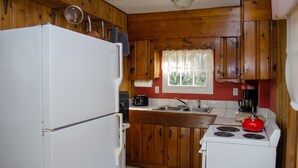 Eine kleine Küche mit Holzausstattung, einem weißen Kühlschrank, einem Herd und einem Spülbecken.