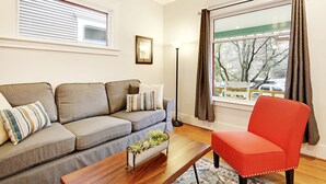 Un salon avec un canapé gris, un fauteuil rouge, une table basse en bois et une fenêtre avec des rideaux.