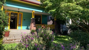 Une maison à deux étages avec un porche, une cheminée en briques et un jardin bien entretenu agrémenté de fleurs violettes.