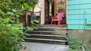 Une terrasse en bois qui mène à un porche agrémenté de deux chaises et d’une plante en pot.