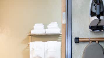 Een badkamer met een toilet, een handdoekhouder met opgevouwen handdoeken, een papieren handdoekdispenser en een strijkijzer op een standaard.