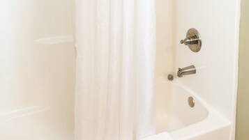 A white bathtub with a shower curtain, a handheld showerhead, and a towel on the side.
