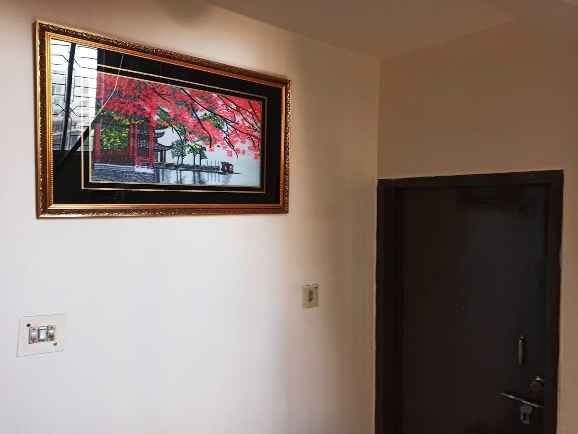 Un quadro incorniciato raffigura un edificio con fogliame rosso su una parete, una porta e un interruttore della luce.