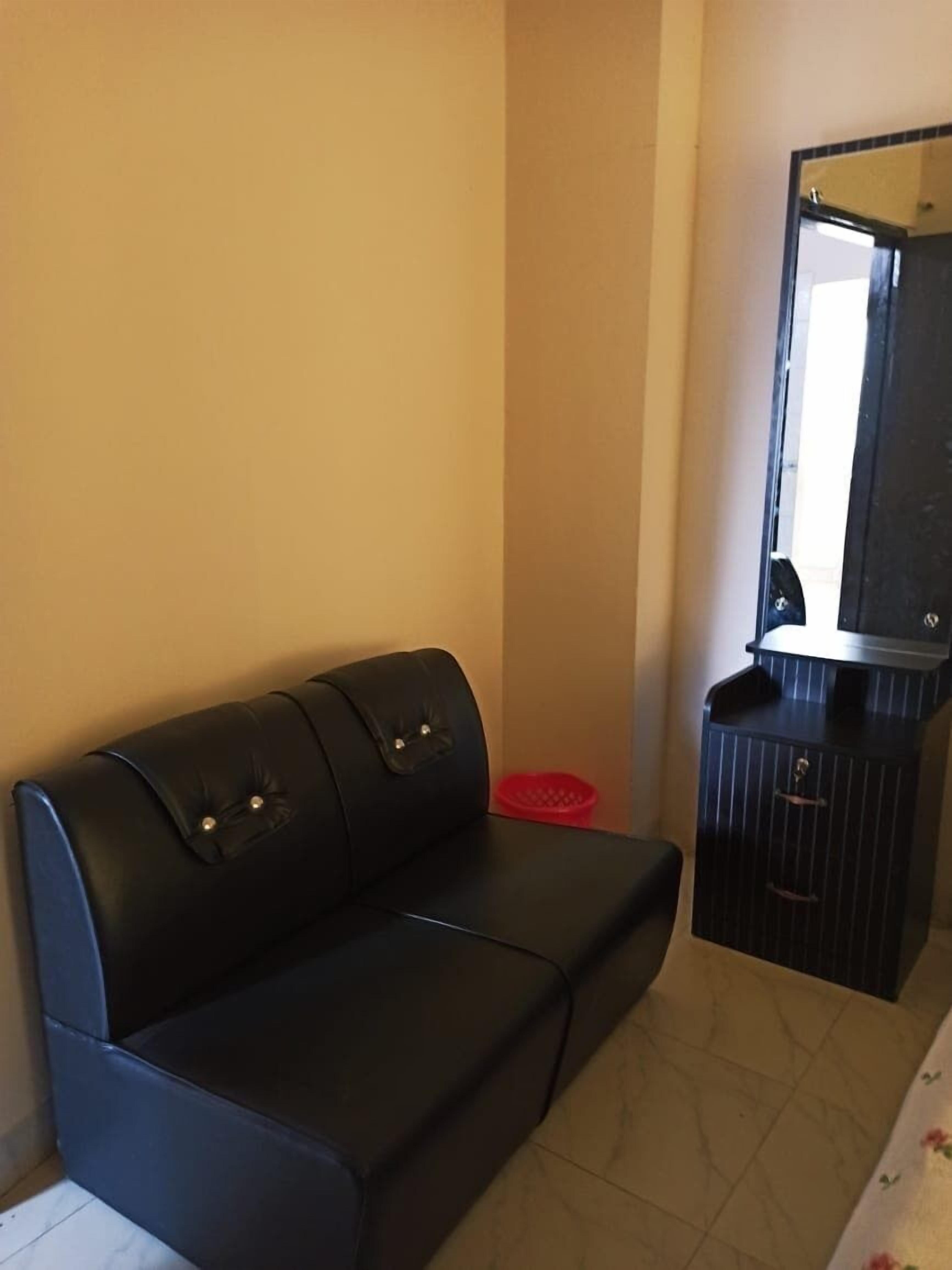 A room with a black leather sofa, a small red basket, and a dark wooden cabinet with a mirror.