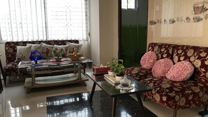 A living room with a sofa, a coffee table, and a dining table. There are potted plants and decorative items on the tables.
