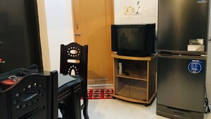 A compact kitchen with a refrigerator, microwave, and a small television on a wooden stand.