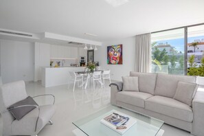 Een moderne woonkamer met een glazen salontafel, een bank en een eethoek met witte stoelen.