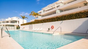 A swimming pool with clear water, surrounded by a white building with balconies and a hedge. - Marbella Golf With Pool Cataleya, Marbella, Spain (Marbella)