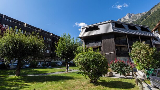 Un bâtiment doté d’un balcon, entouré d’arbres, avec une montagne en arrière-plan.