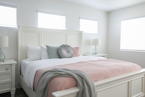Une chambre à coucher bien rangée, avec un lit blanc, une table de chevet et une petite table d’appoint.