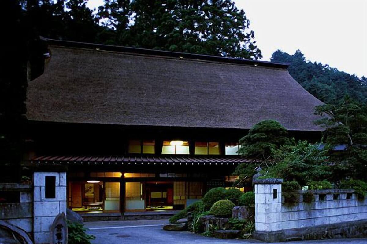 Een traditioneel Japans gebouw met een betegeld dak, een stenen entree en een goed onderhouden tuin.