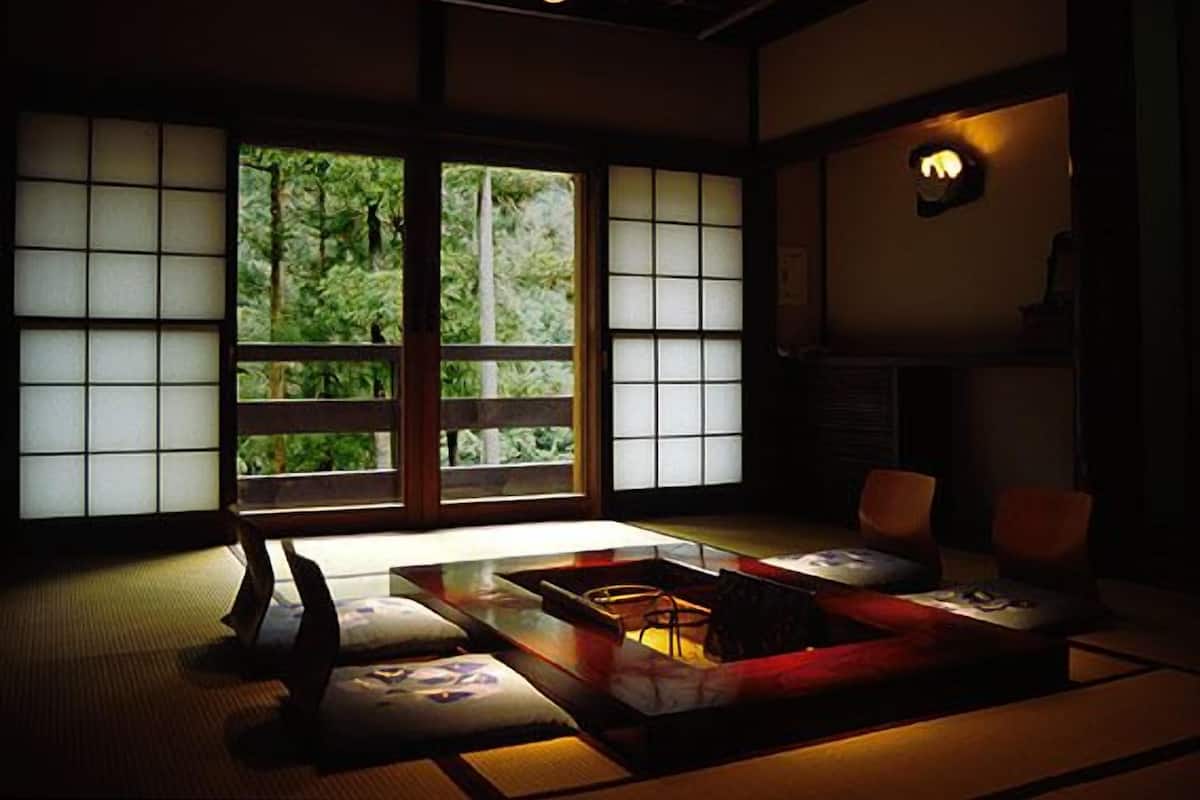 Een traditionele Japanse kamer met tatami vloeren, een lage tafel, kussens en een schuifdeur met uitzicht op groen.