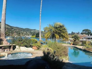 A pool area with a hot tub, palm trees, and a view of a lake and hills. - Luxury Tranquil Waterfront Haven w/Pool & Spa (San Rafael)