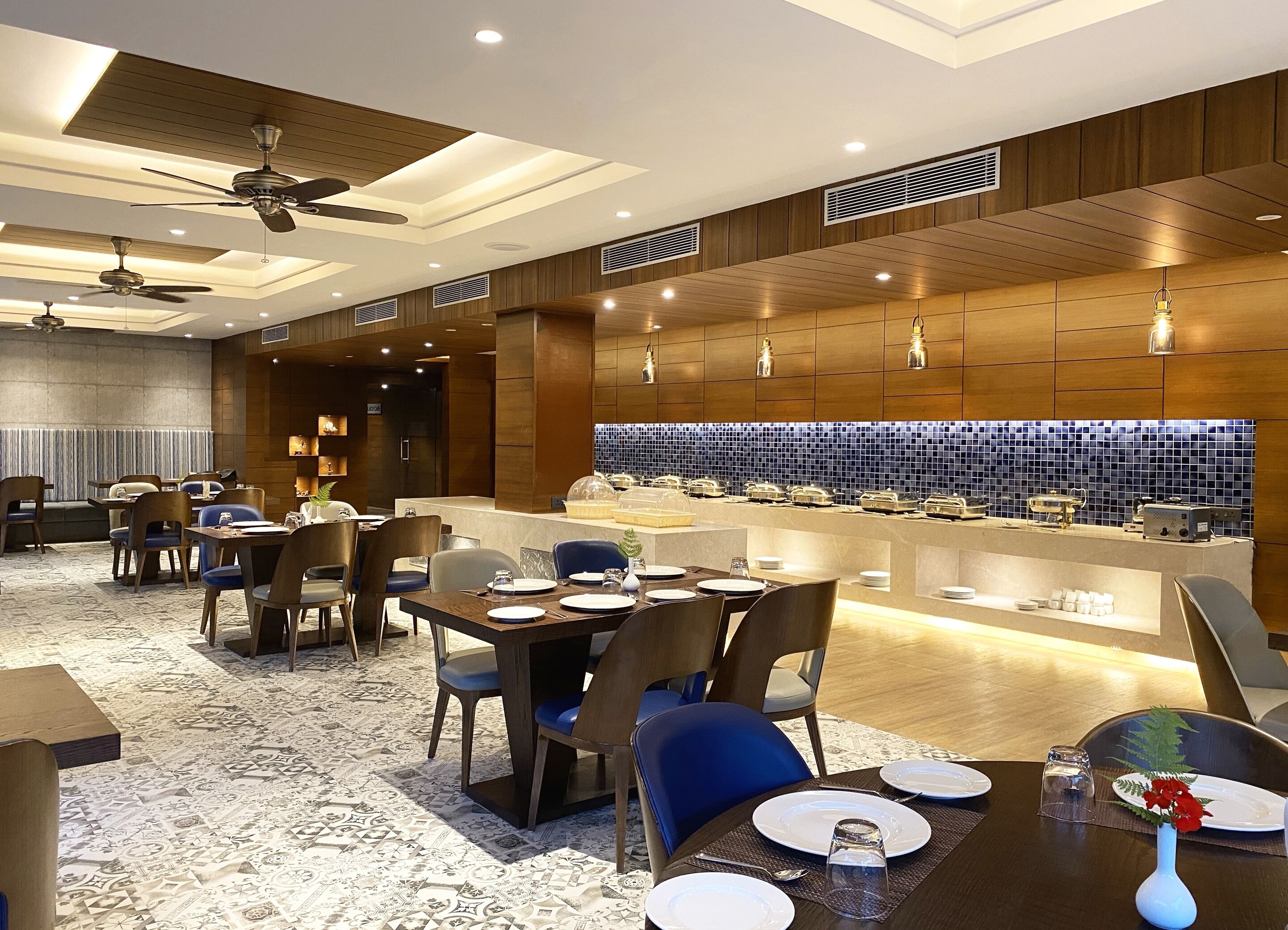 A modern dining area with a buffet setup, ceiling fans, and a patterned carpet.