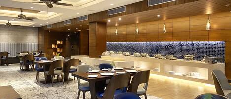 A modern dining area with a buffet setup, ceiling fans, and a patterned carpet.