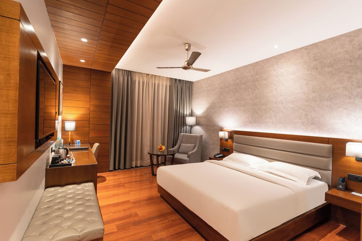 Ein Hotelzimmer mit einem großen Bett, einem Schreibtisch mit Stuhl, einem kleinen Tisch mit Lampe und einem Deckenventilator.