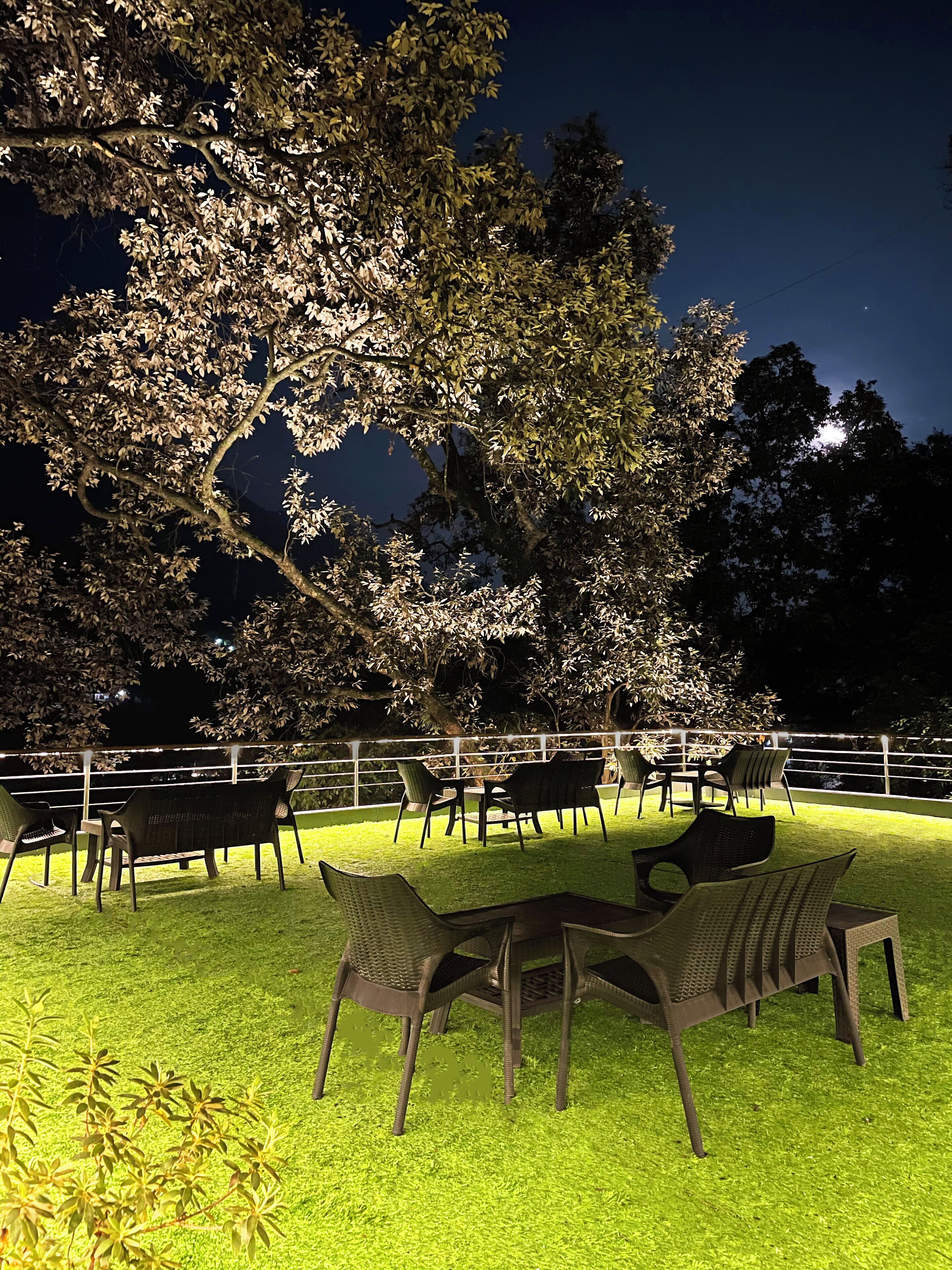 An outdoor seating area with chairs and tables, surrounded by trees and a railing.
