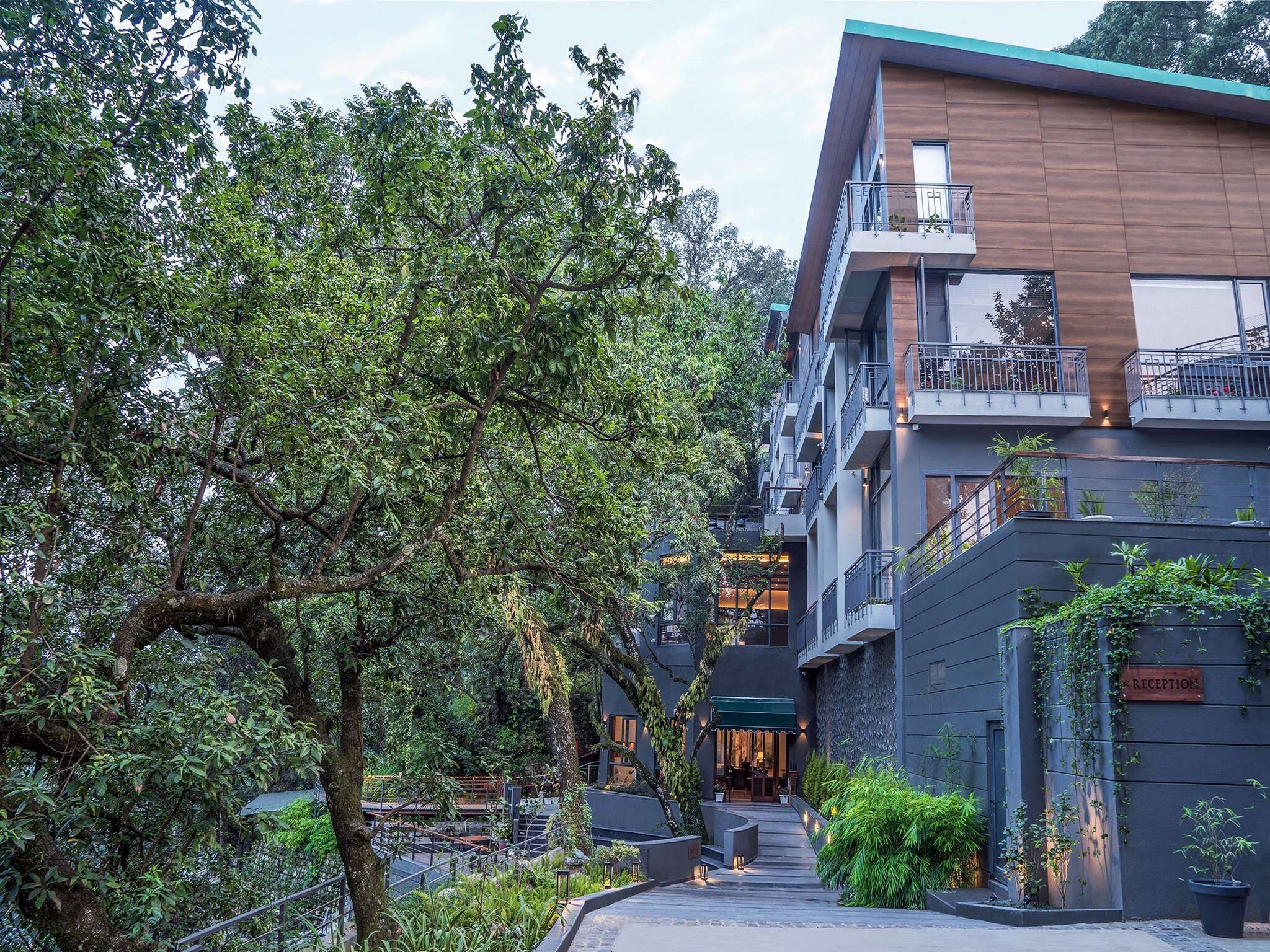 A modern building with multiple balconies, a reception area, and lush greenery surrounding the structure.