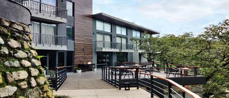 A modern building with a stone facade, outdoor seating area, and a staircase leading to the upper levels.