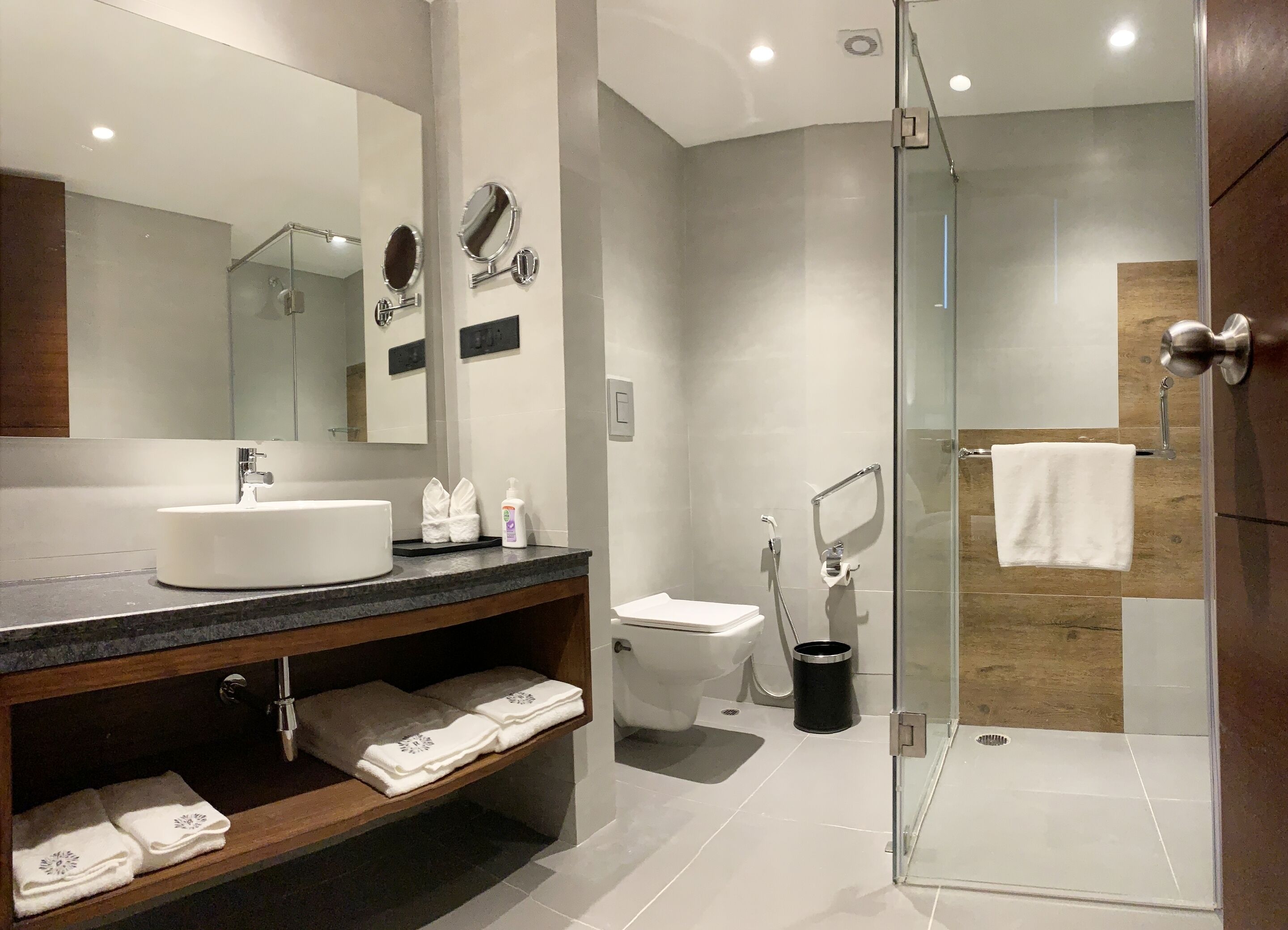 Un baño moderno con un espejo grande, un lavamanos, un inodoro y una zona de ducha con mampara de vidrio.