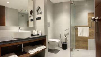 Un baño moderno con un espejo grande, un lavamanos, un inodoro y una zona de ducha con mampara de vidrio.