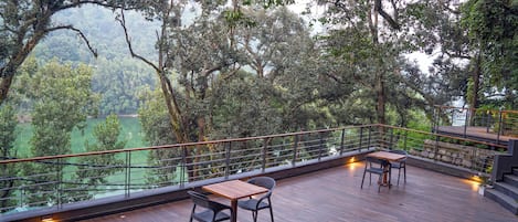 Una terraza de madera con dos mesas y sillas, con vista a un paisaje verde exuberante.