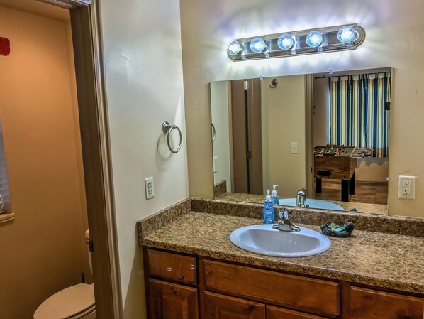 A bathroom with a granite countertop, a white sink, a mirror with lights, and a wooden vanity.