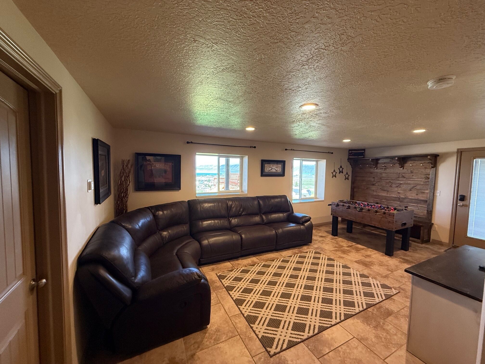 A living room with a leather sectional sofa, a foosball table, and a kitchen area.