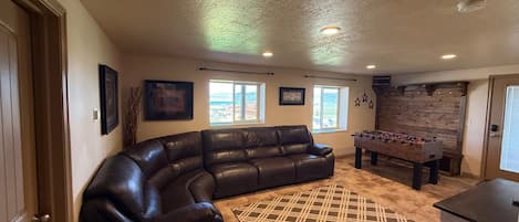 A living room with a leather sectional sofa, a foosball table, and a kitchen area.