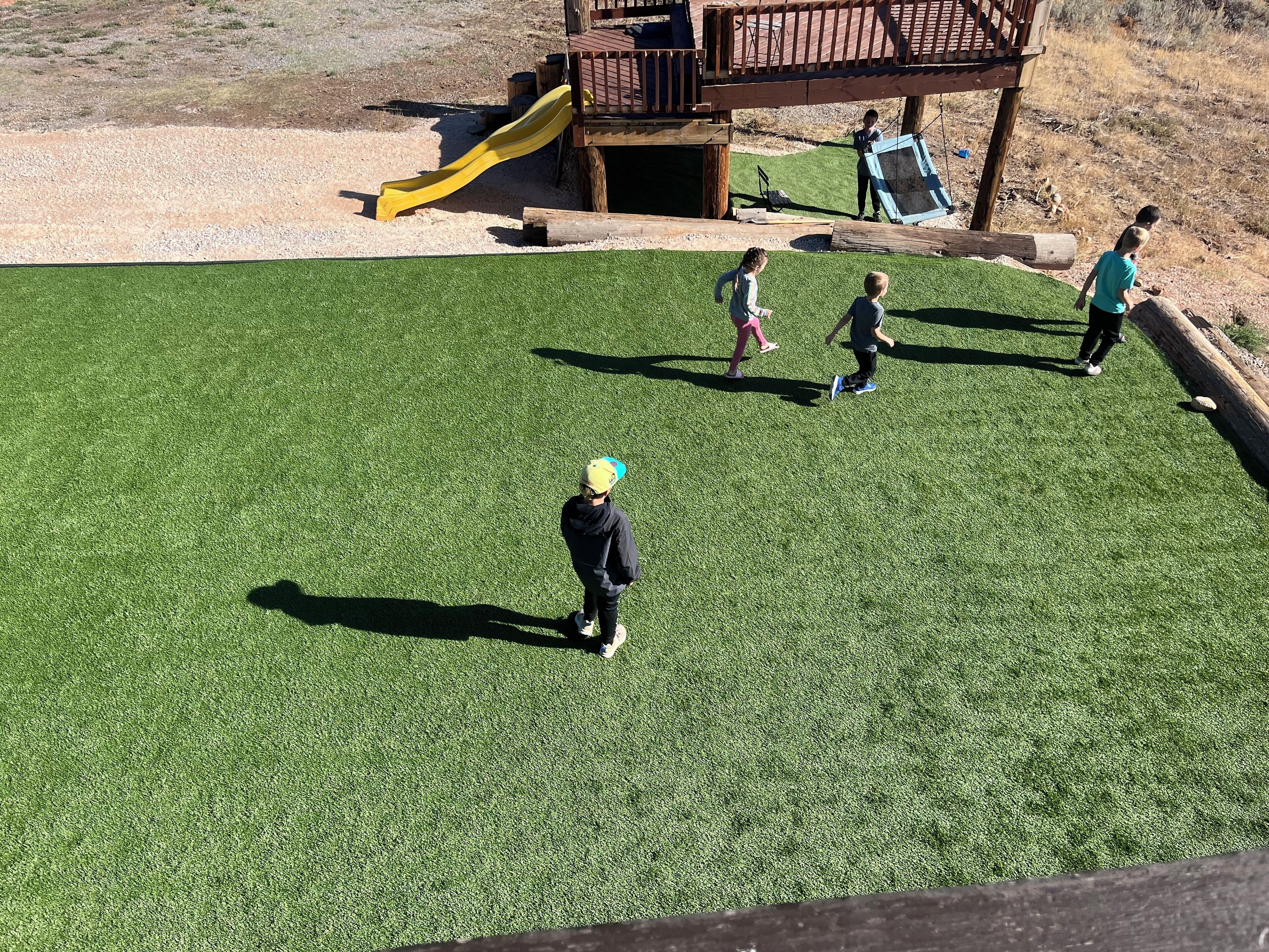 A grassy outdoor area with a wooden play structure and a slide.