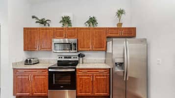 A kitchen with wooden cabinets, a stainless steel refrigerator, a microwave, an oven, and a toaster.