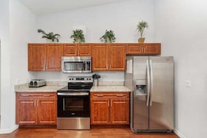 Una cocina con gabinetes de madera, un refrigerador de acero inoxidable, un microondas, un horno y un tostador.