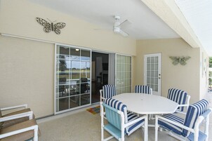 An outdoor patio with a white table and striped chairs, a sliding glass door, and a ceiling fan.