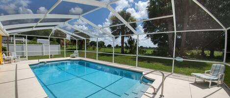 A covered swimming pool with a view of a grassy area and trees.