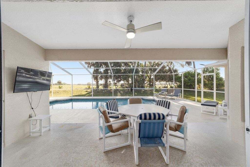 A modern outdoor dining area with a pool, white furniture, and a ceiling fan.