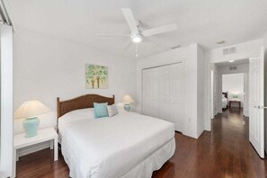A bedroom with a bed, nightstands, a ceiling fan, and a door.