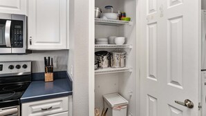Une cuisine avec des meubles blancs, un four à micro-ondes, une cuisinière et un plan de travail muni d’un bloc à couteaux.