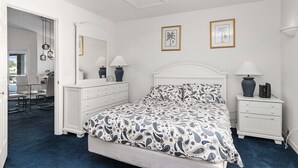 Une chambre à coucher comprenant un lit, deux tables de chevet, une commode, un miroir et deux tableaux encadrés accrochés au mur.