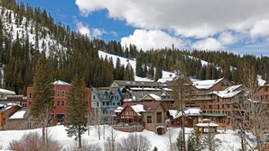 Une ville de montagne enneigée, avec un télésiège, des bâtiments en bois et un ciel dégagé.