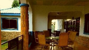 A covered outdoor dining area with a table and chairs, a wooden column, and a view of a building with a blue roof. - Classy Holiday Villas With Pool in Accra, Ghana (Tema)