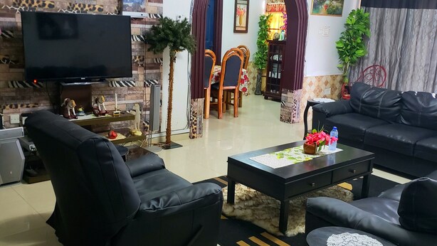A living room with a flat-screen TV, black leather sofas, a coffee table, and a dining area with a wooden table and chairs. - Classy Holiday Villas With Pool in Accra, Ghana (Tema)